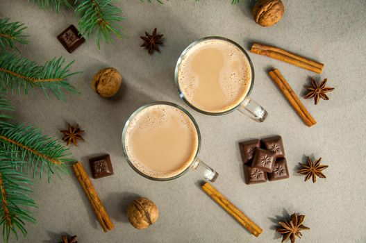 Hot Christmas Drink Cocoa Coffee or Chocolate with Milk in a Small Transparent Cup. Fir Tree Branch, Nuts, Cinnamon Sticks Star Anise on a Grey Background. Top View Winter time. New Year