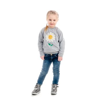 Little blonde child smiling awkwardly, wearing blue jeans and gray sweatshirt, isolated on white background