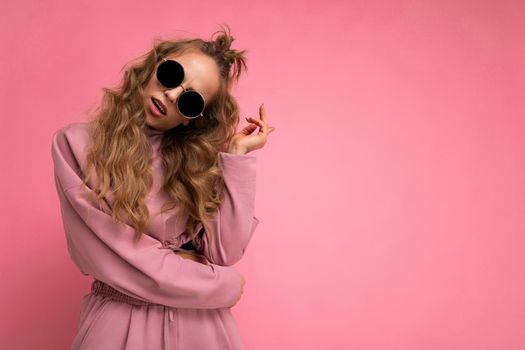 Photo shot of beautiful young dark blonde woman wearing casual clothes and stylish sunglasses isolated over colorful background looking at camera. copy space