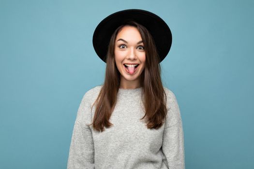 Portrait of cute attractive pretty young happy positive brunette woman wearing casual striped sweater isolated over colorful background with copy space and showing tongue.