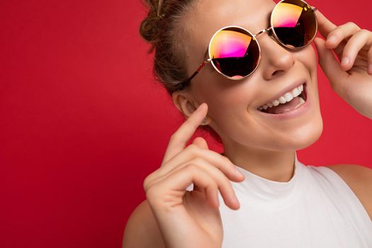 Closeup portrait photo of attractive positive smiling young blonde woman wearing everyday stylish clothes and modern sunglasses isolated on colorful background wall looking at camera.