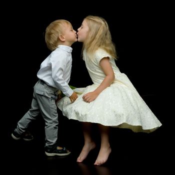 Brother and sister, girl and boy kissing each other in the studio on a black background. The concept of family values, happy childhood.