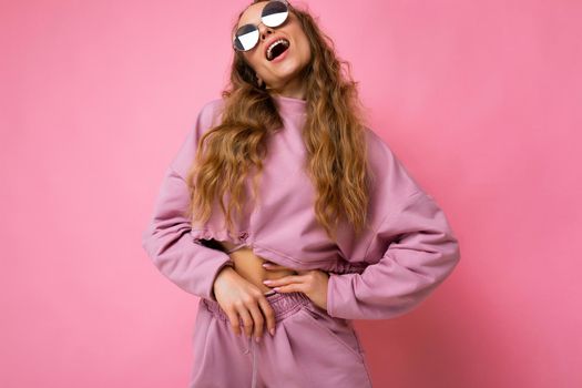 Photo of pretty positive young blonde curly woman isolated over pink background wall wearing casual pink sport clothes and stylish sunglasses looking up.