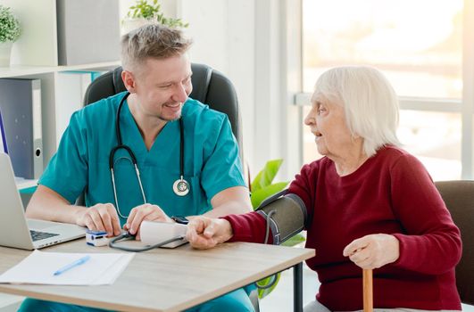 Doctor measuring blood pressure of elderly patient using tonometer during appointment in clinic