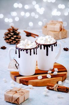 Christmas Hot Drink. White Cups of Cocoa or Chocolate with Marshmallows and Spices Cinnamon on Light Background with Christmas Decorations and Lights of Bokeh.