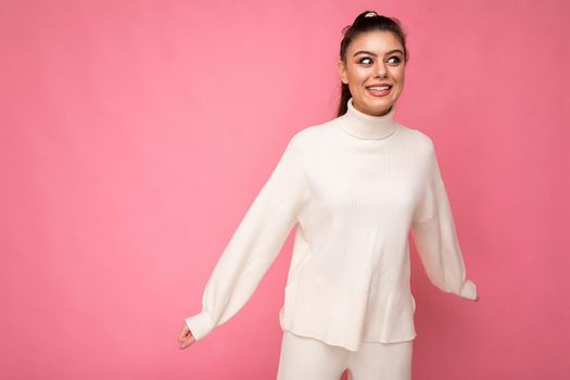 Young beautiful happy positive smiling stylish brunette woman wearing casual white sweater poising isolated on pink background wall. Fun and joy concept. Copy space.
