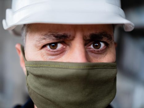 Close-up of a male construction worker in a construction helmet and protective medical mask on a construction site. Gradual exit from quarantine. The opening of the construction sites.