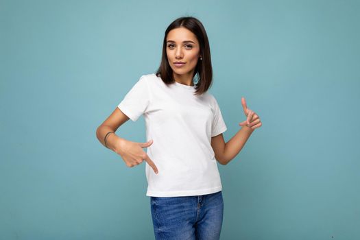 Attractive self-confident young brunette woman in casual white t-shirt for mockup isolated on blue background with free space.