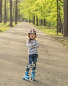 Little girl in helmet standing in the alley, roller blading, arms crossed on chest