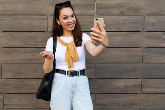 Photo of beautiful young woman wearing casual clothes standing in the street having communication via mobile phone looking at smartphone and having fun and good mood.Copy space