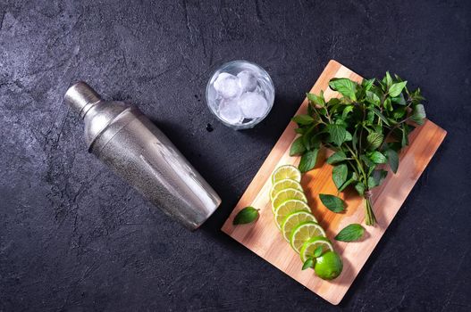 Mojito Cocktail Making. Mint, Lime, Ice, Glass and Bar Shaker on Dark Stone Table. Copy Space For Your Text.