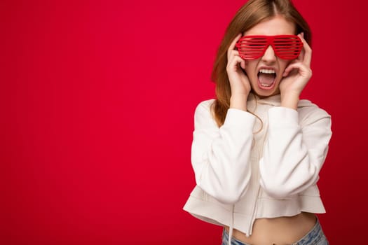 Photo shot of beautiful positive young blonde woman wearing casual clothes and stylish optical glasses isolated over colorful background wall looking at camera and having fun. copy space