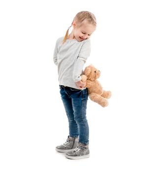 Small girl peaking on a teddy bear hidden behind her back, isolated on white background