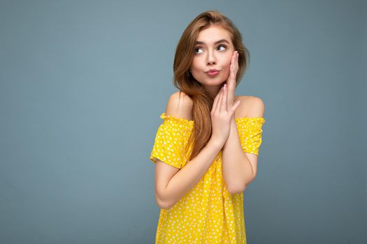 Young cute beautiful dark blonde woman with sincere emotions isolated on background wall with copy space wearing stylish yellow dress. Positive concept.