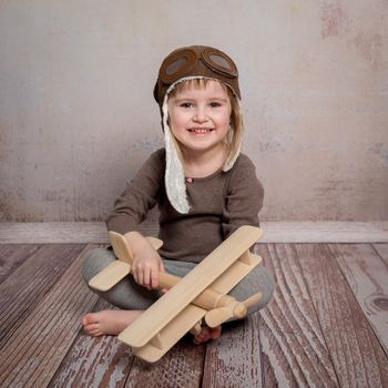 smiling little girl with wooden plane in hands sitting on the floor