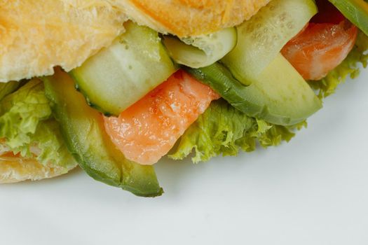 Croissant sandwich with red fish, avocado, fresh vegetables and arugula on black shale board over black stone background. Healthy food concept.