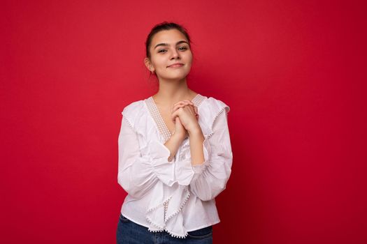 Portrait of positive cheerful fashionable woman in formalwear holding two hands together looking at camera isolated on red background with copy and empty space.