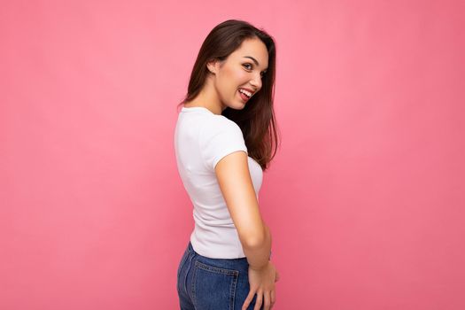 Young beautiful brunet woman. Trendy lady in casual summer white t-shirt. Positive female shows facial sincere emotions. Funny model isolated on pink background with free space.