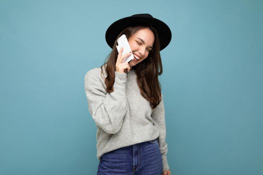 a young girl in a hat speaks on the phone against a blue wall.