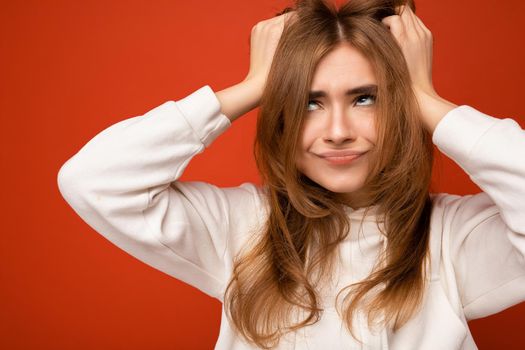 Photo of emotional sat adult beautiful dark blonde woman with sincere emotions isolated on background wall with copy space wearing casual white hoodie.