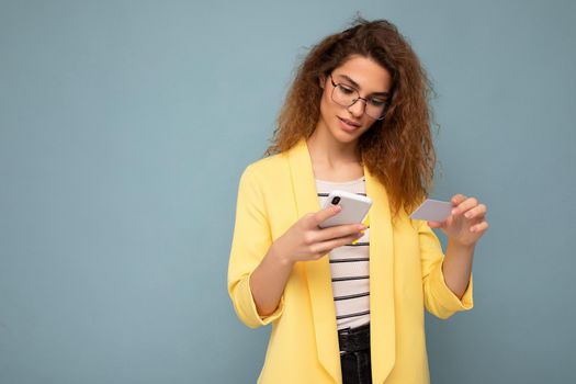 Young woman wearing everyday clothes isolated over background holding phone and credit card paying online shopping through credit card looking at smartphone screen.