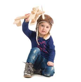 cute little girl in pilot hat with wooden plane in hand isolated on white background