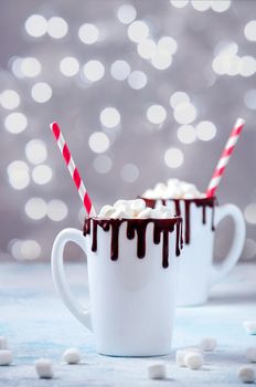 Christmas Hot Drink. White Cups of Cocoa or Chocolate with Marshmallows on Light Background with Christmas Decorations and Lights of Bokeh.