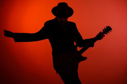 silhouette of guitarist in a hat on a red background.