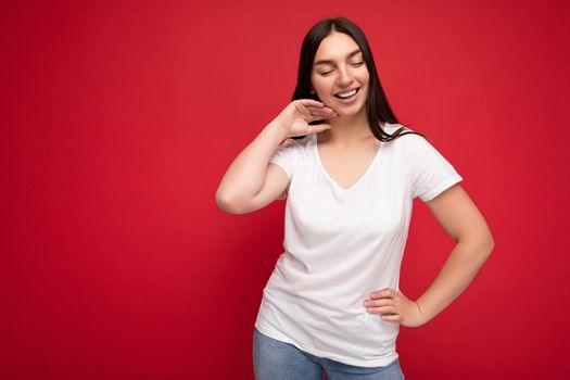 Young happy attractive brunette woman with sincere emotions isolated on background wall with copy space wearing casual white t-shirt for mockup. Positive concept.