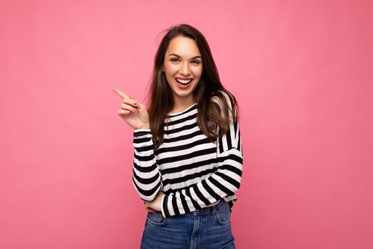 Portrait of beautiful fascinating emotional positive joyful happpy female promoter pointing to the side at copy space for advertising wearing hipster outfit isolated over background wall with empty space with sincere emotions.