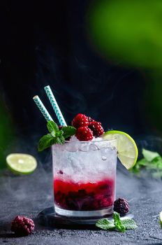 Alcoholic Cocktail with Rum or Vodka, Soda, Raspberry and Blackberry Puree, Lime and Mint in the Glass with Smoke on the Dark Grey Background.