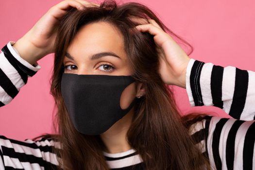 Shot portrait of young brunette attractive woman wearing mediacal face mask isolated over background wall. Protection against COVID-19.