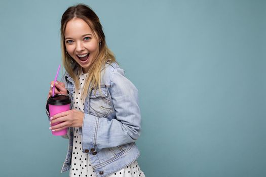 Beautiful young positive blonde woman wearing casual stylish clothes isolated over colorful background wall holding paper cup for mockup drinking coffee looking at camera. copy space