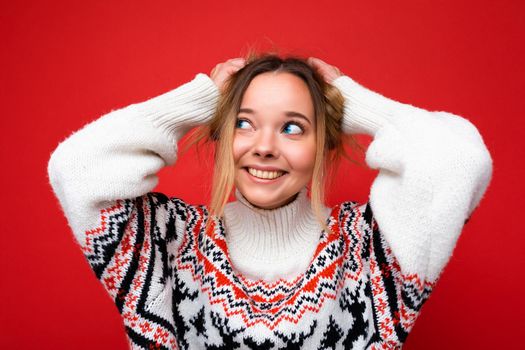 Young beautiful woman. Trendy woman in casual winter sweater. Positive female shows facial emotions. Funny model isolated on red background.