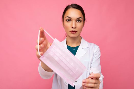 Beautiful young woman holds and wears a white medical mask to protect yourself from corona virus, cares for her health and safety, sticks to self-isolation. Concept of Covid-19.