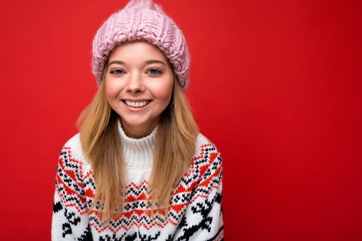 Attractive smiling happy young blonde woman standing isolated over colorful background wall wearing everyday stylish outfit showing facial emotions looking at camera.