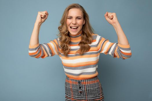 Photo of young positive happy smiling beautiful woman with sincere emotions wearing stylish clothes isolated over background with copy space and celebrating victory.
