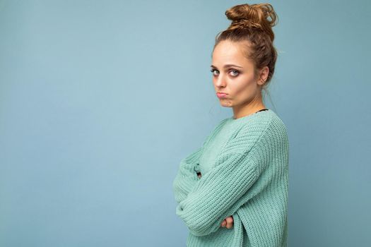 Shot of young upset touchy offended pretty blonde woman wearing blue jersey isolated on blue background with empty space.