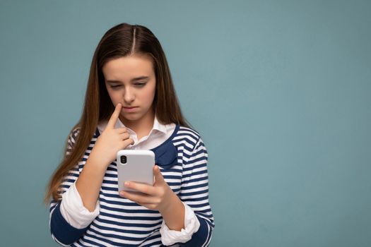 Beautiful young girl wearing casual clothes standing isolated over background surfing on the internet via phone looking at mobile screen.