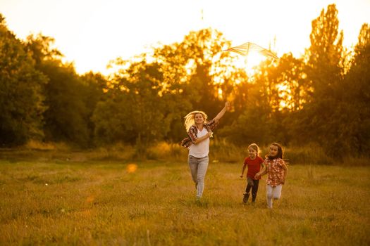 happy family mother and children run on meadow with a kite in the summer on the nature