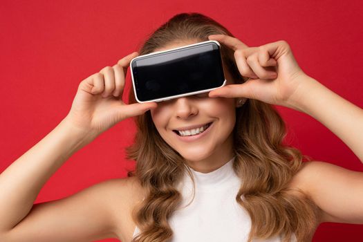 closeup Photo of beautiful smiling young woman good looking wearing casual stylish outfit standing isolated on background with copy space holding smartphone showing phone in hand with empty screen display for mockup.