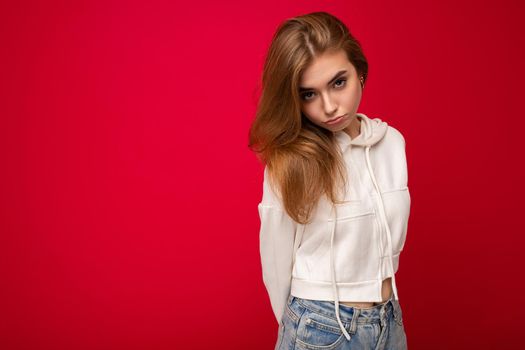 Young offended beautiful dark blonde woman with sincere emotions isolated on background wall with copy space wearing casual white hoodie. Sad concept.