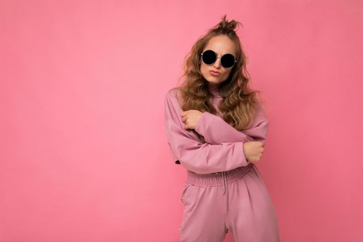 Photo shot of beautiful positive young dark blonde woman wearing casual clothes and stylish sunglasses isolated over colorful background looking at camera. empty space