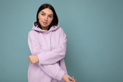 Young beautiful brunette woman with sincere emotions isolated on background wall with copy space wearing casual stylish purple hoodie. Positive concept.