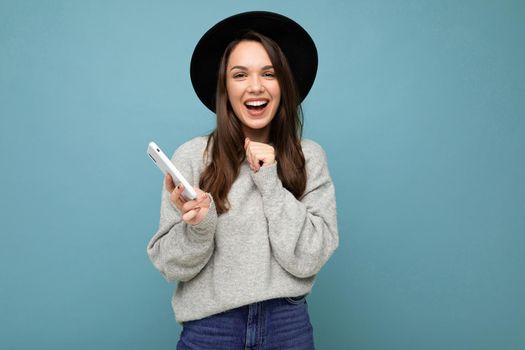 Image of a happy young beautiful woman posing isolated over blue wall background using mobile phone.