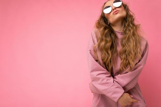 Attractive amusing young blonde woman wearing everyday stylish clothes and modern sunglasses isolated on colorful background wall looking up and having fun. copy space