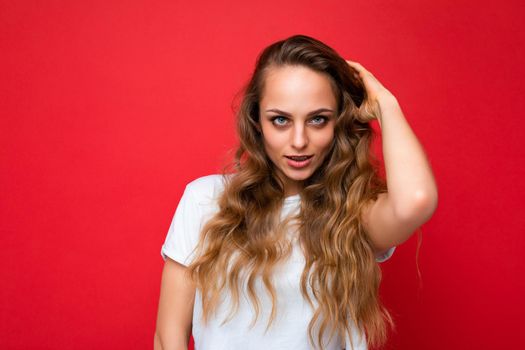 Young beautiful curly blonde woman with sexy expression, cheerful and happy face wearing casual white t-shirt isolated over red background with copy space.