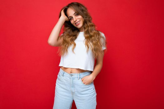 Young beautiful curly blonde woman with sexy expression, cheerful and happy face wearing casual white t-shirt isolated over red background with copy space.