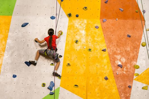 Sporty little girl climbing artificial boulder on practical wall in gym