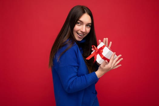 Shot of attractive positive smiling young brunette woman isolated over colourful background wall wearing everyday trendy outfit holding gift box and looking at camera.